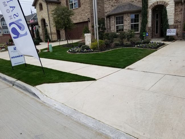Stone building entrance with landscaped lawn, sidewalks, and a banner sign by the curb