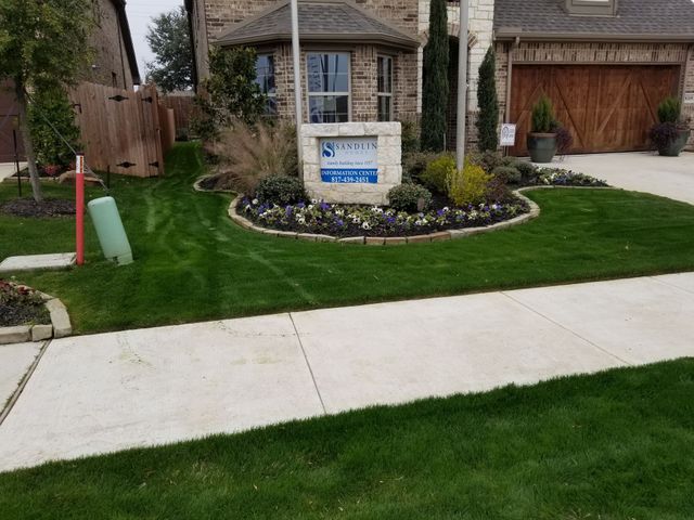 Suburban house entrance with a stone sign, landscaped lawn, and sidewalk along the street