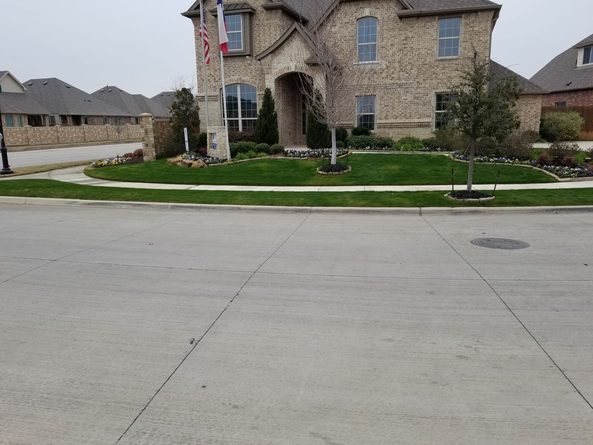 Suburban street with a stone house, sidewalk, and manicured lawn across the road