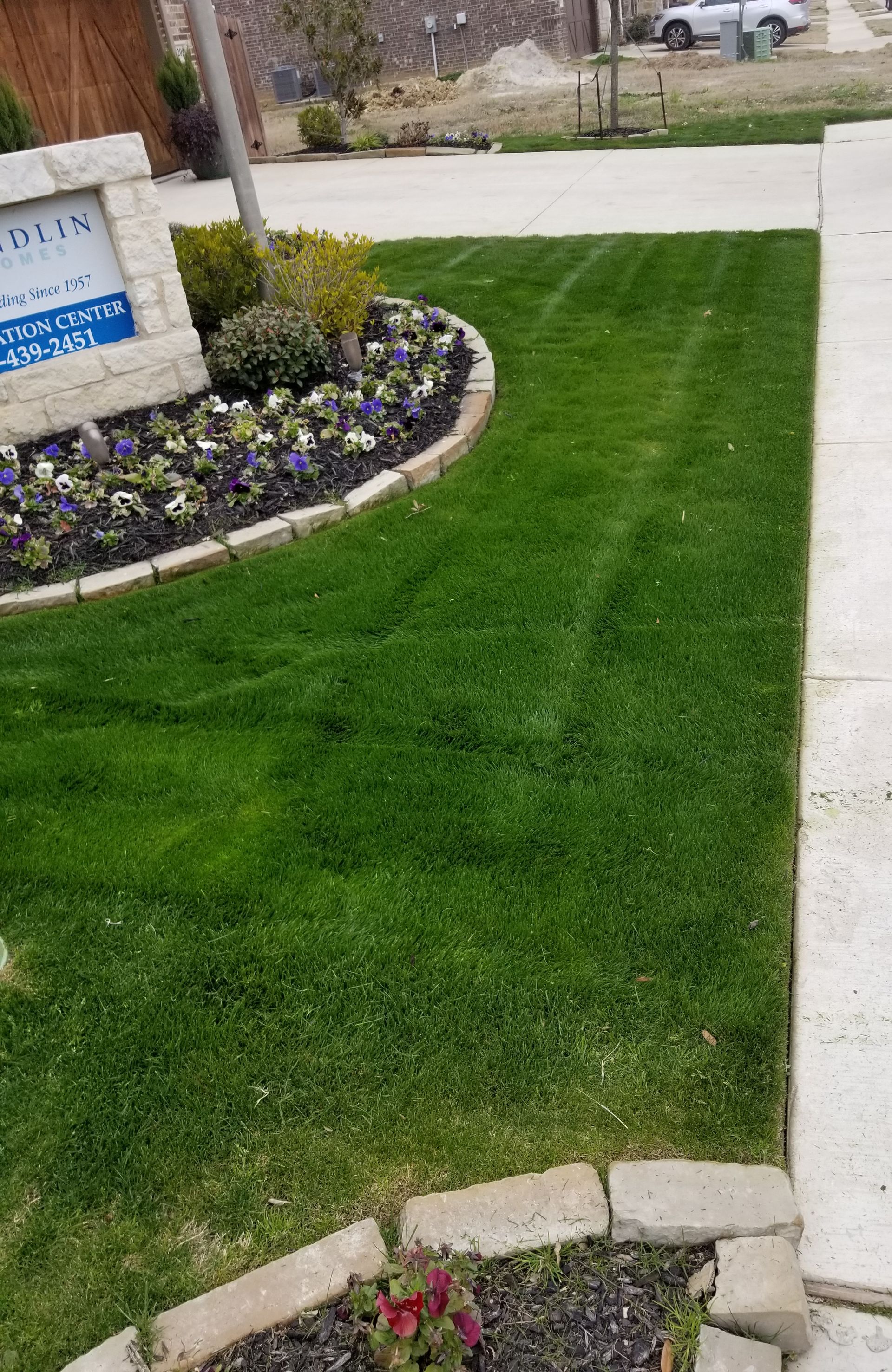 Lush green lawn beside a stone flower bed and sidewalk at a residential entrance.