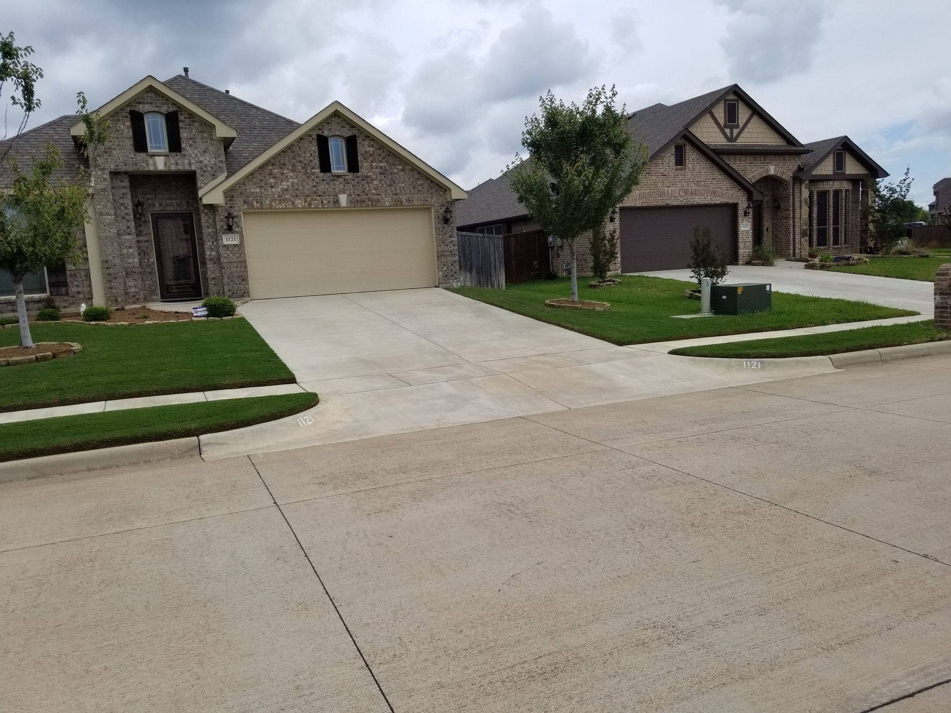 Suburban homes with stone facades and a wide concrete driveway under a cloudy sky