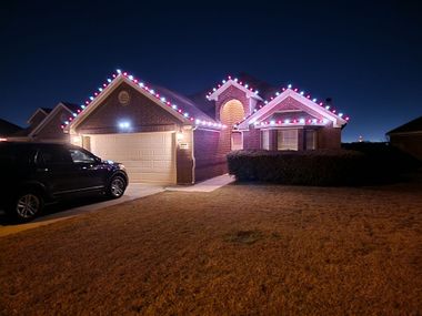 Suburban house at night with pink holiday lights and a black SUV in the driveway