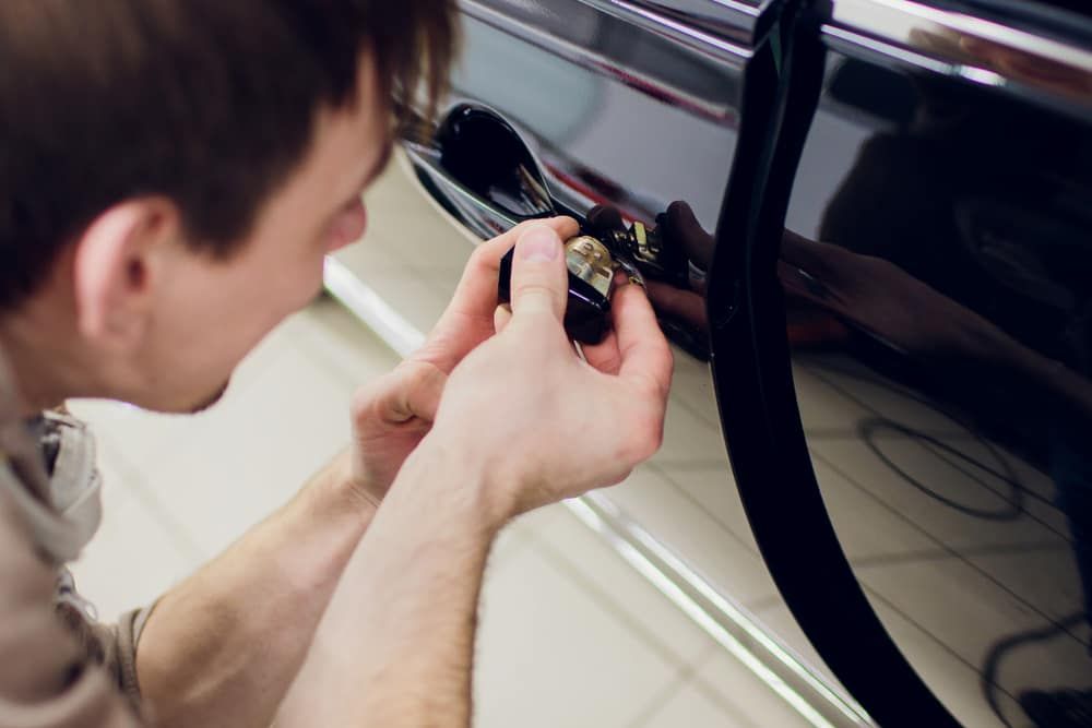 a Man is Holding a Key in Front of a Car Door — Armstrong Locksmiths Ballarat In Bacchus Marsh, VIC