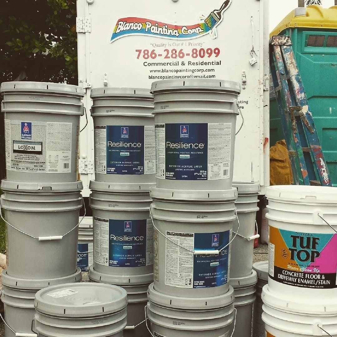 Paint buckets stacked near a truck with a painting company logo and a porta-potty.