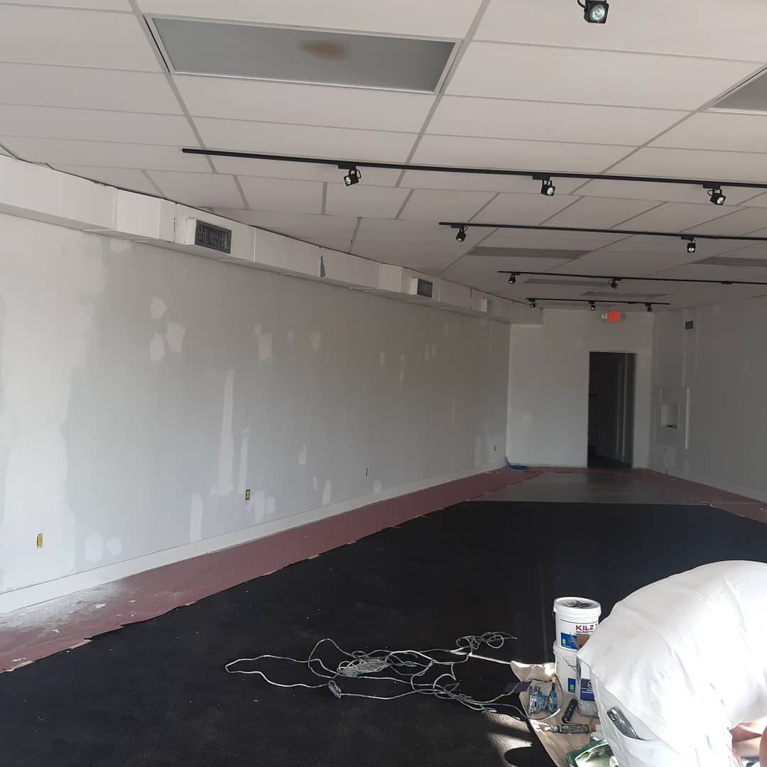 Empty interior space with white walls and dark floor. A person is working on the right.