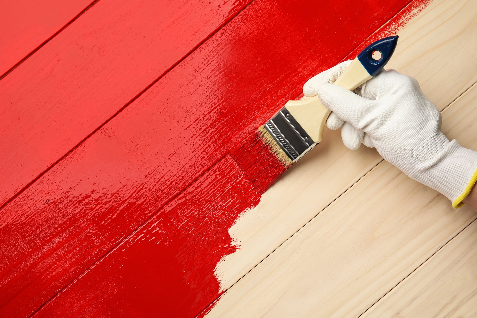 Hand with paintbrush applying red paint to wooden planks.