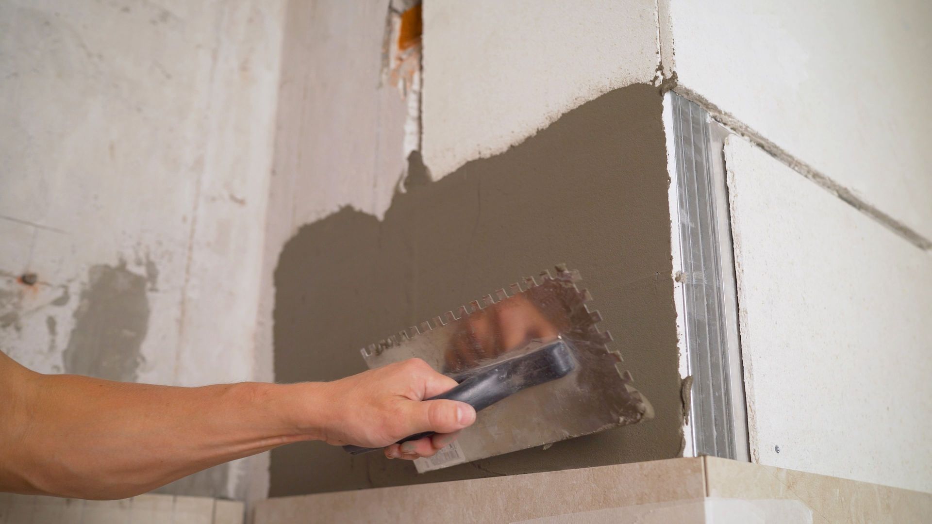 Person using a trowel to apply gray plaster to a corner wall.