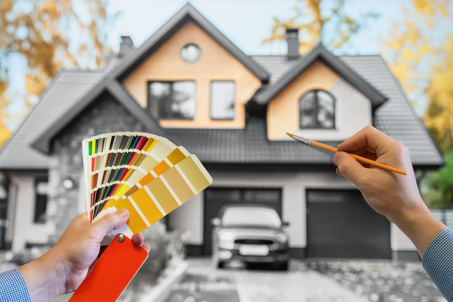 Hands hold paint swatches and brush in front of a house, selecting paint colors for exterior.