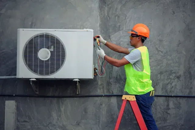 HVAC technician performing air conditioner repair and maintenance on outdoor AC unit.