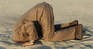 A man is kneeling down in the sand with his head in the sand.