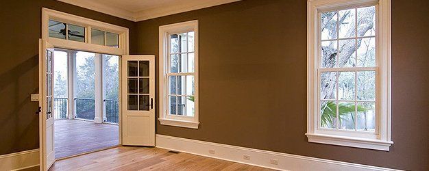 An empty room with brown walls and white trim and two windows.