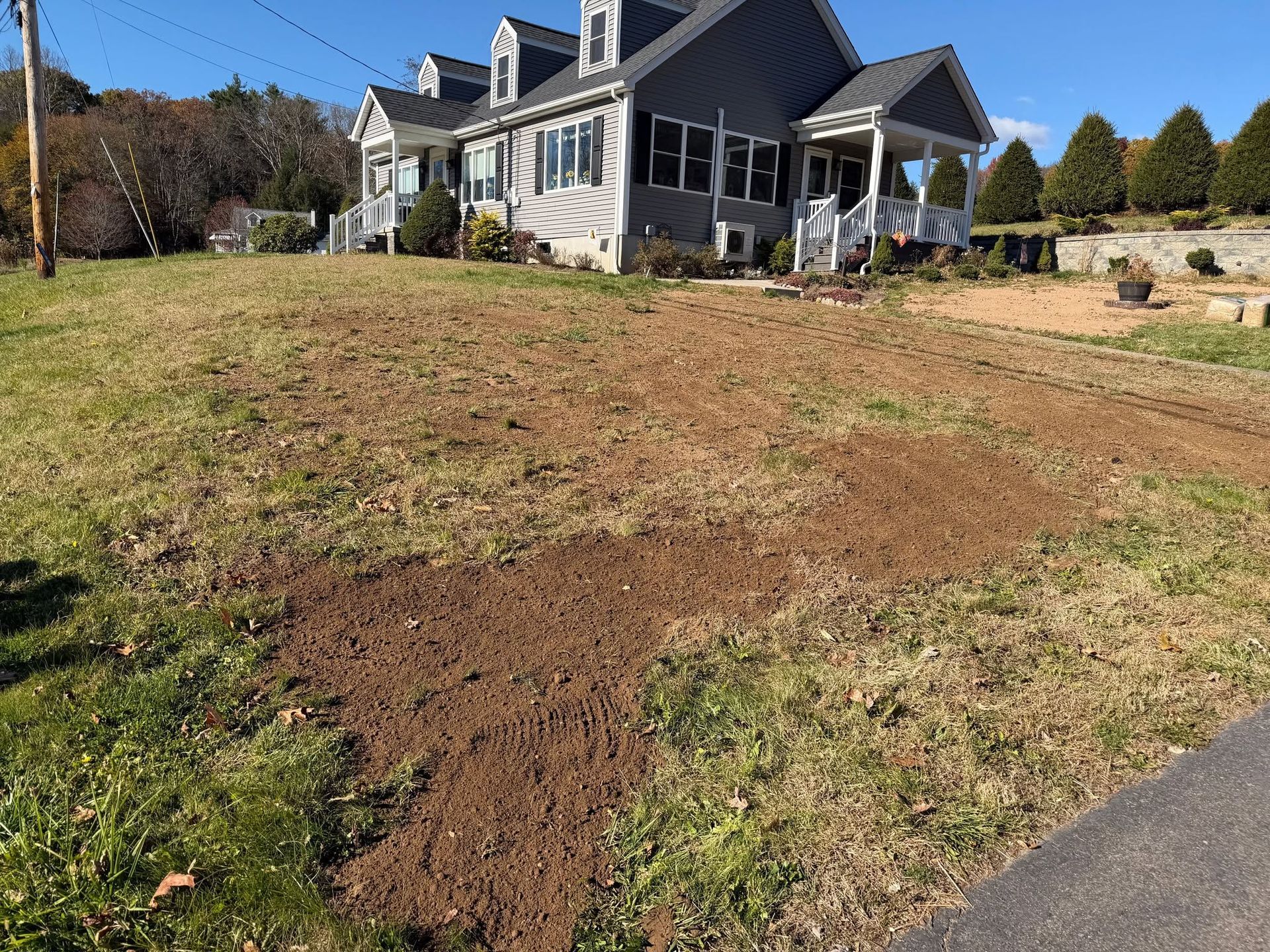 House on a sloped yard with exposed soil and a patchy lawn beside a driveway.