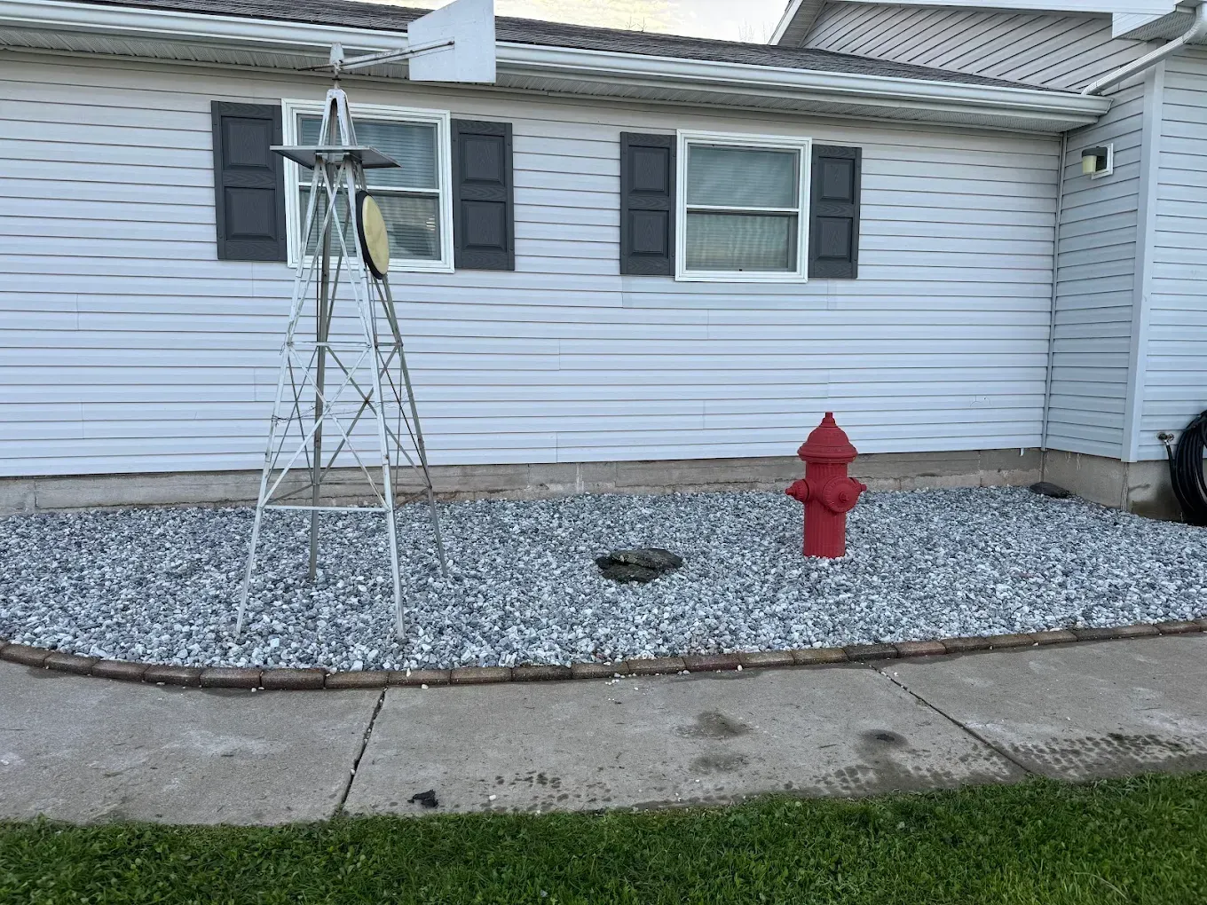 House exterior with white siding, black shutters, red fire hydrant, and a small metal tree in a gravel bed