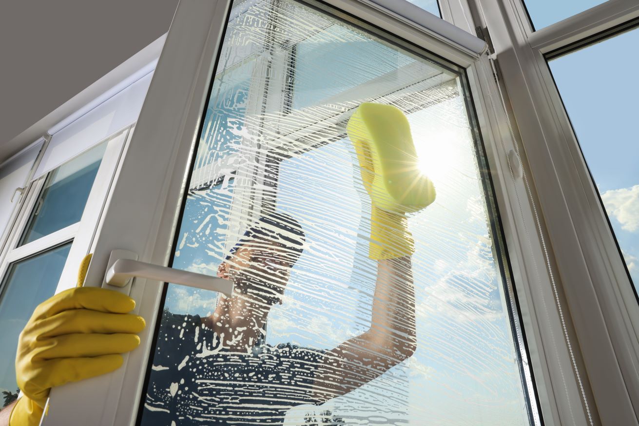 A Person Wearing Yellow Gloves Is Cleaning A Window With A Sponge