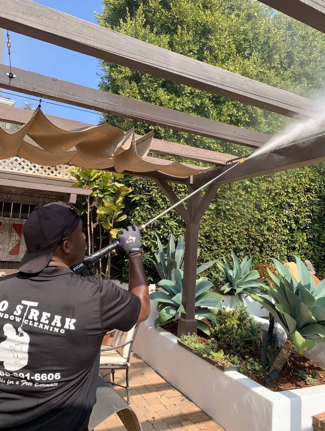 A Man Is Cleaning A Pergola With A High Pressure Washer
