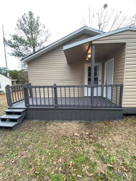 Wooden deck with gray railings and steps, attached to a house with tan siding.