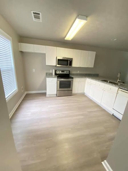 Empty kitchen with stainless steel appliances, white cabinets, and wood-look flooring.
