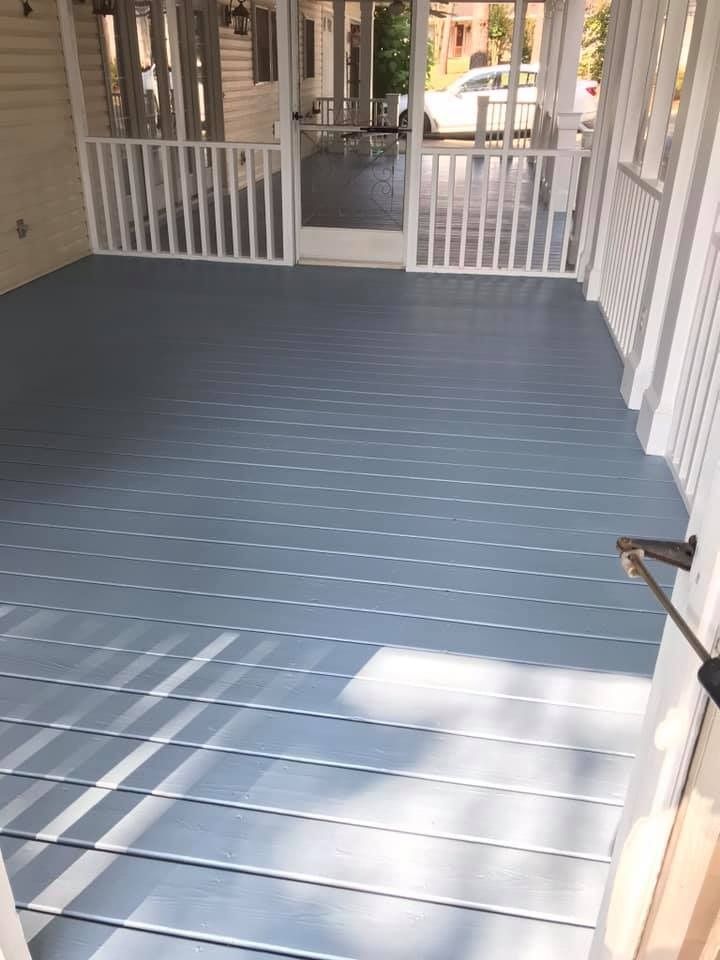 Blue painted porch with white railing and open door, sunny setting.