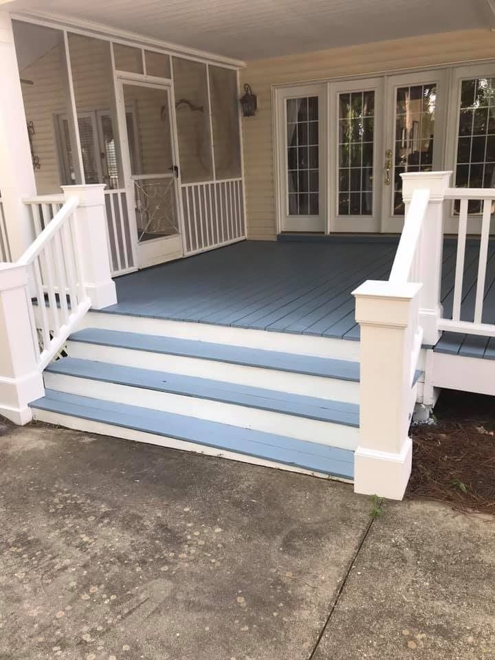 Deck with blue flooring and white railings leading to screened porch and double doors.