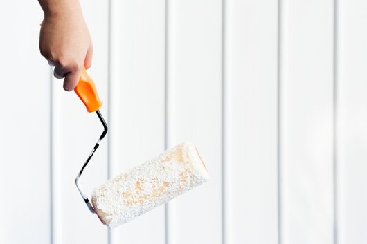 Hand holding a paint roller with white paint against a white paneled surface.