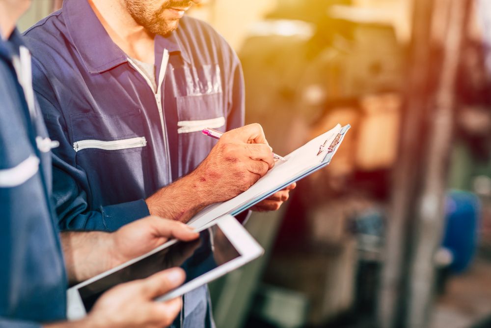 Two men are looking at a tablet and a clipboard.