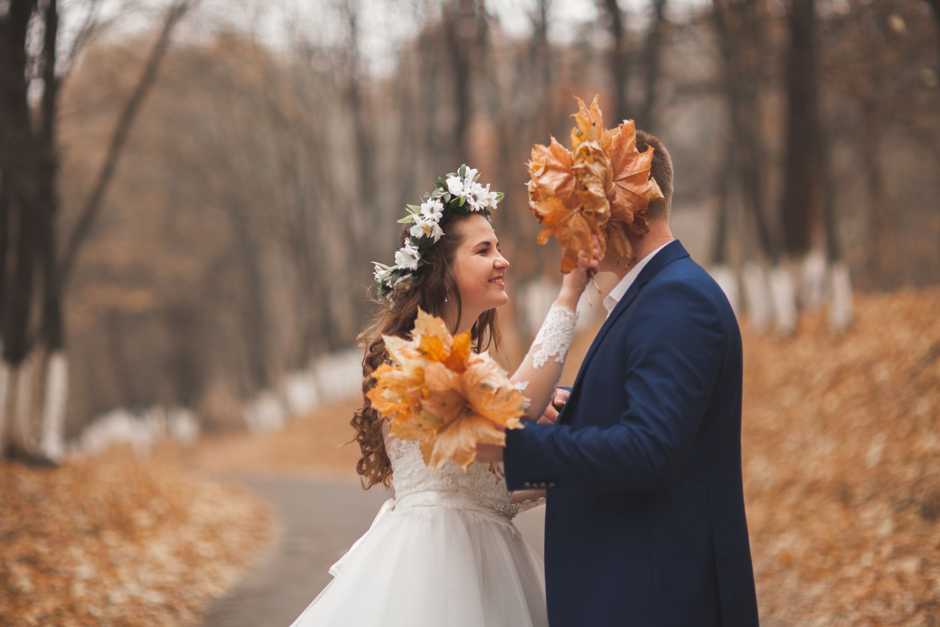 Bride and groom sharing autumn leaves on a tree-lined path