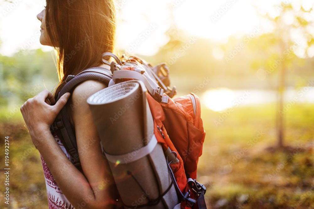 A woman is carrying a backpack and a yoga mat on her back.