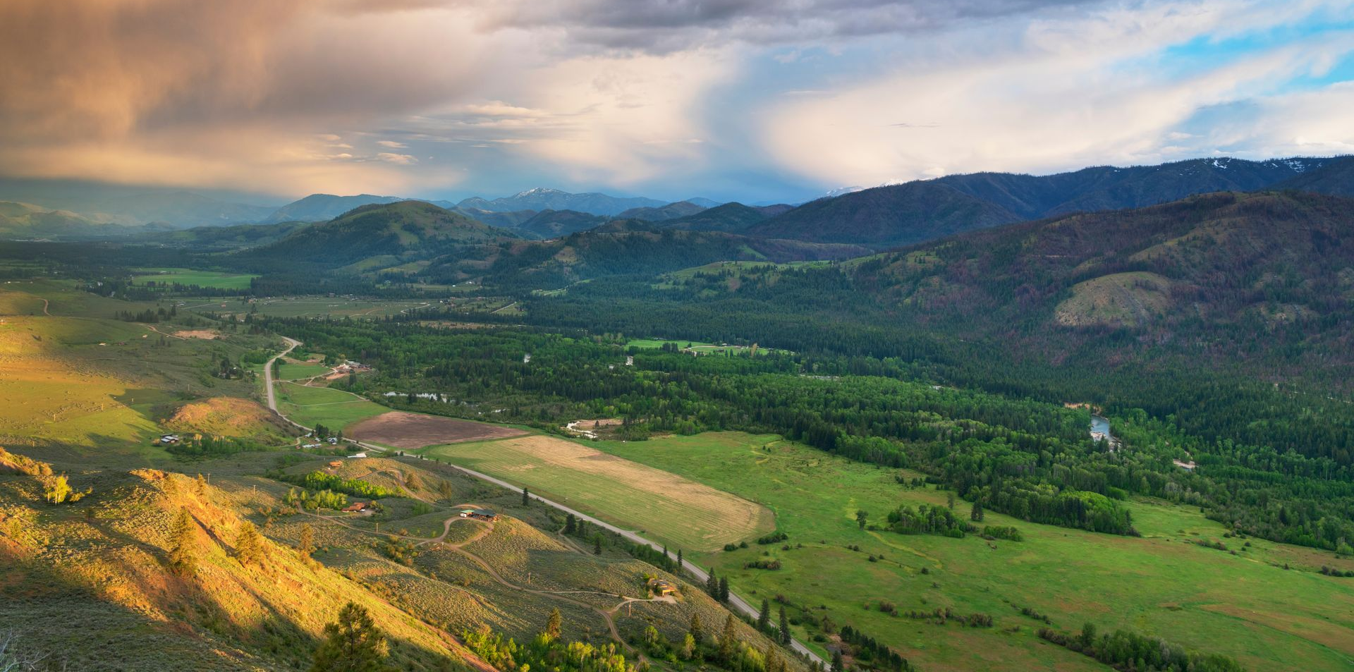 Lush green valley with winding river, terraced fields, and mountains under a cloudy sky