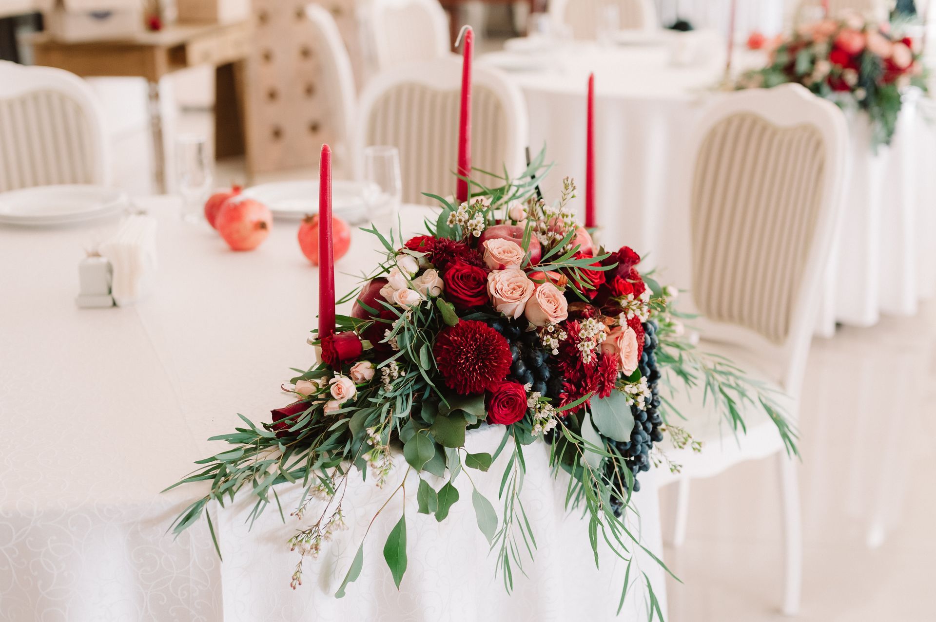 Floral centerpiece with red candles on a white table at a decorated event