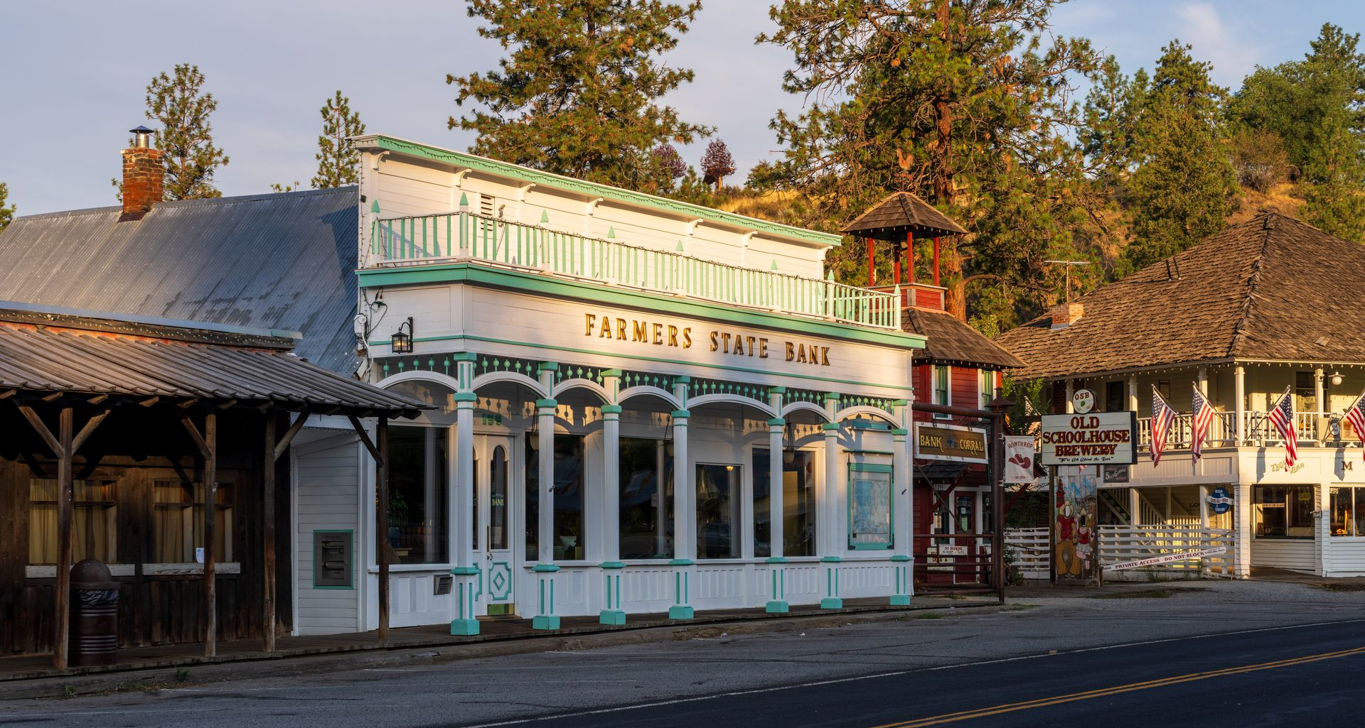 Old Western storefronts on a quiet street at sunset, including a white building with a green sign.