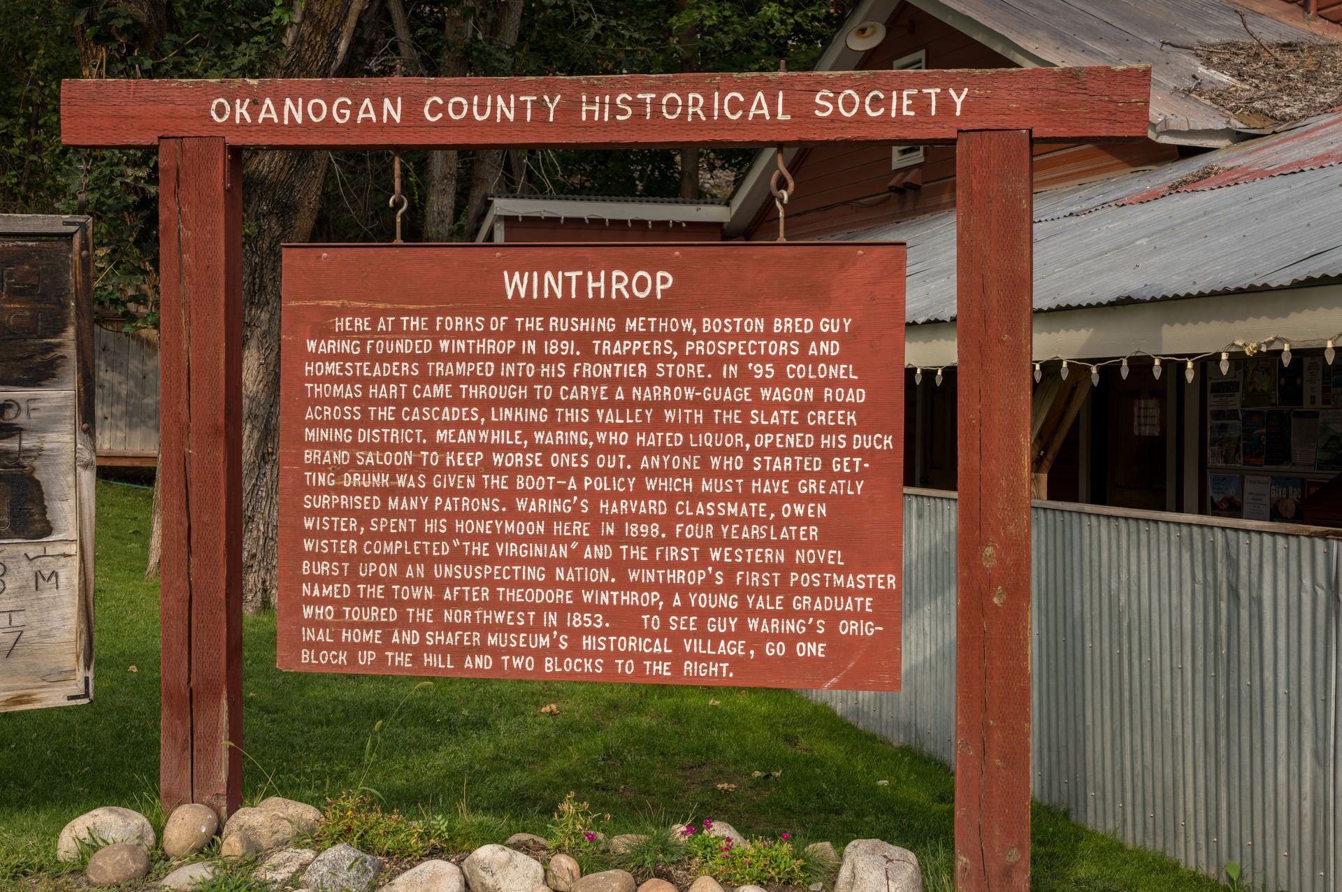 Okanagan County Historical Society signboard with red wooden frame and informational plaque outdoors