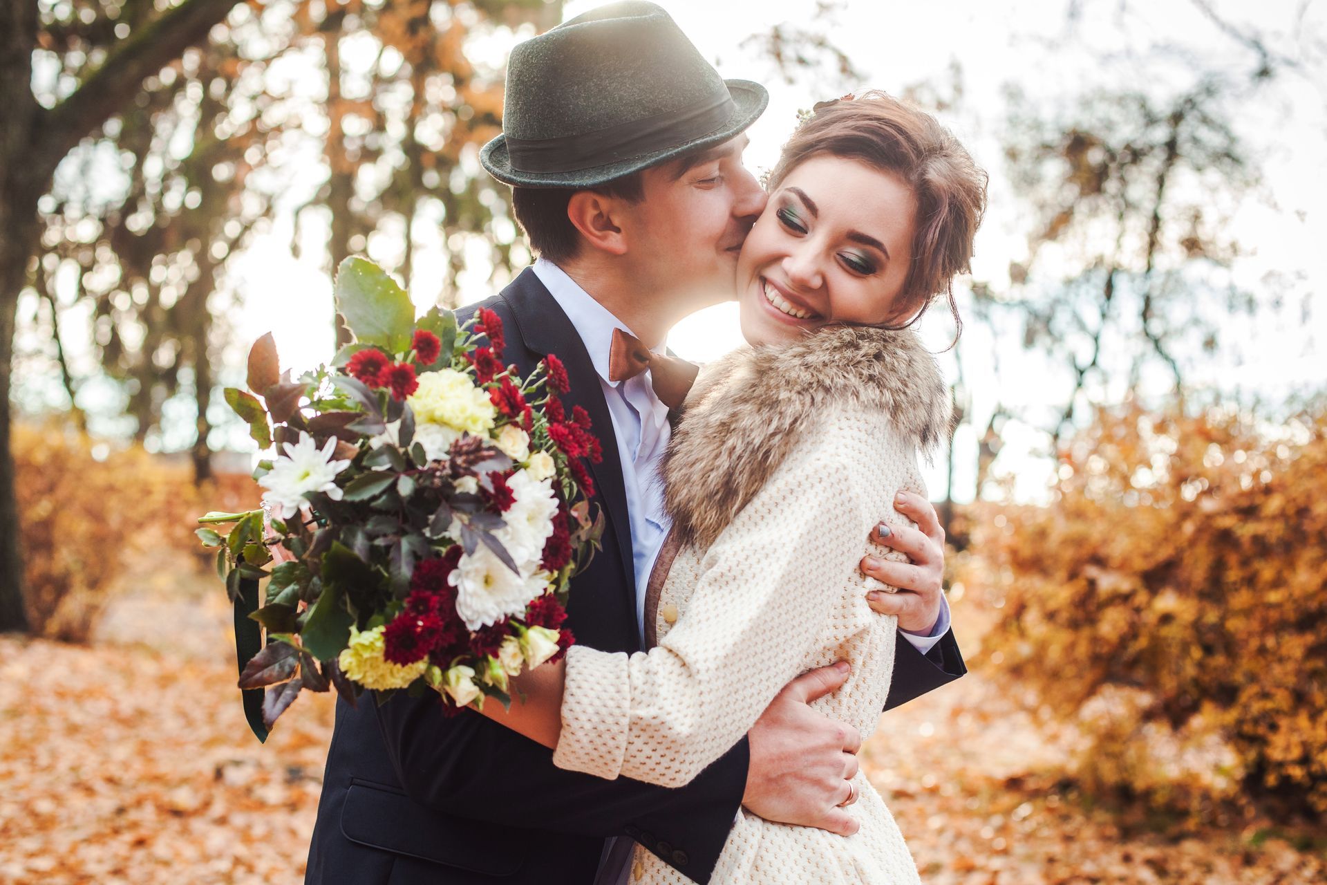 Couple embracing outdoors, smiling with a bouquet in autumn light
