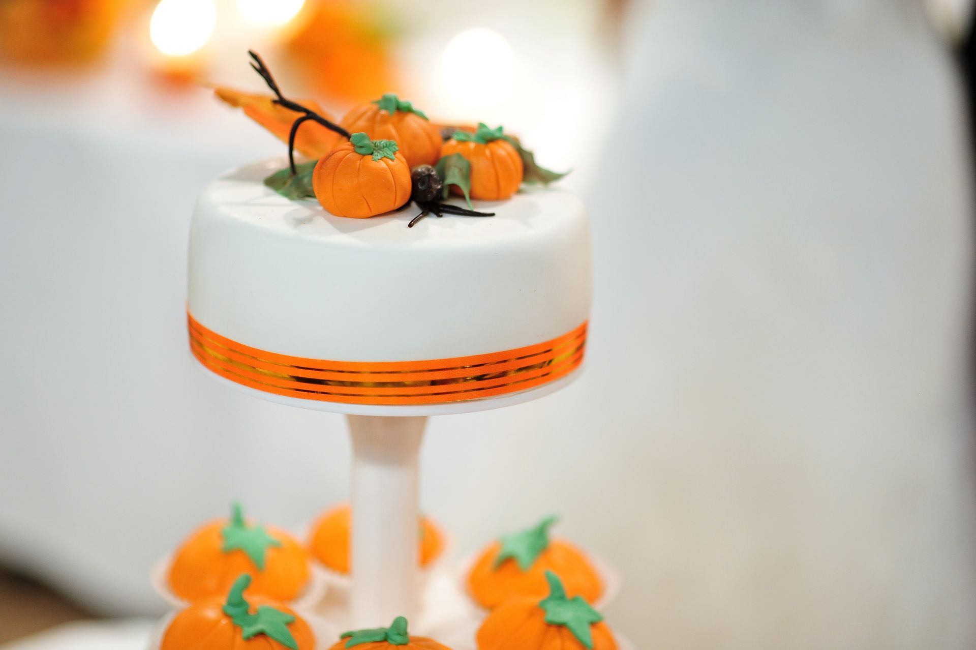White cake with orange ribbon and pumpkin decorations on a stand for a fall celebration