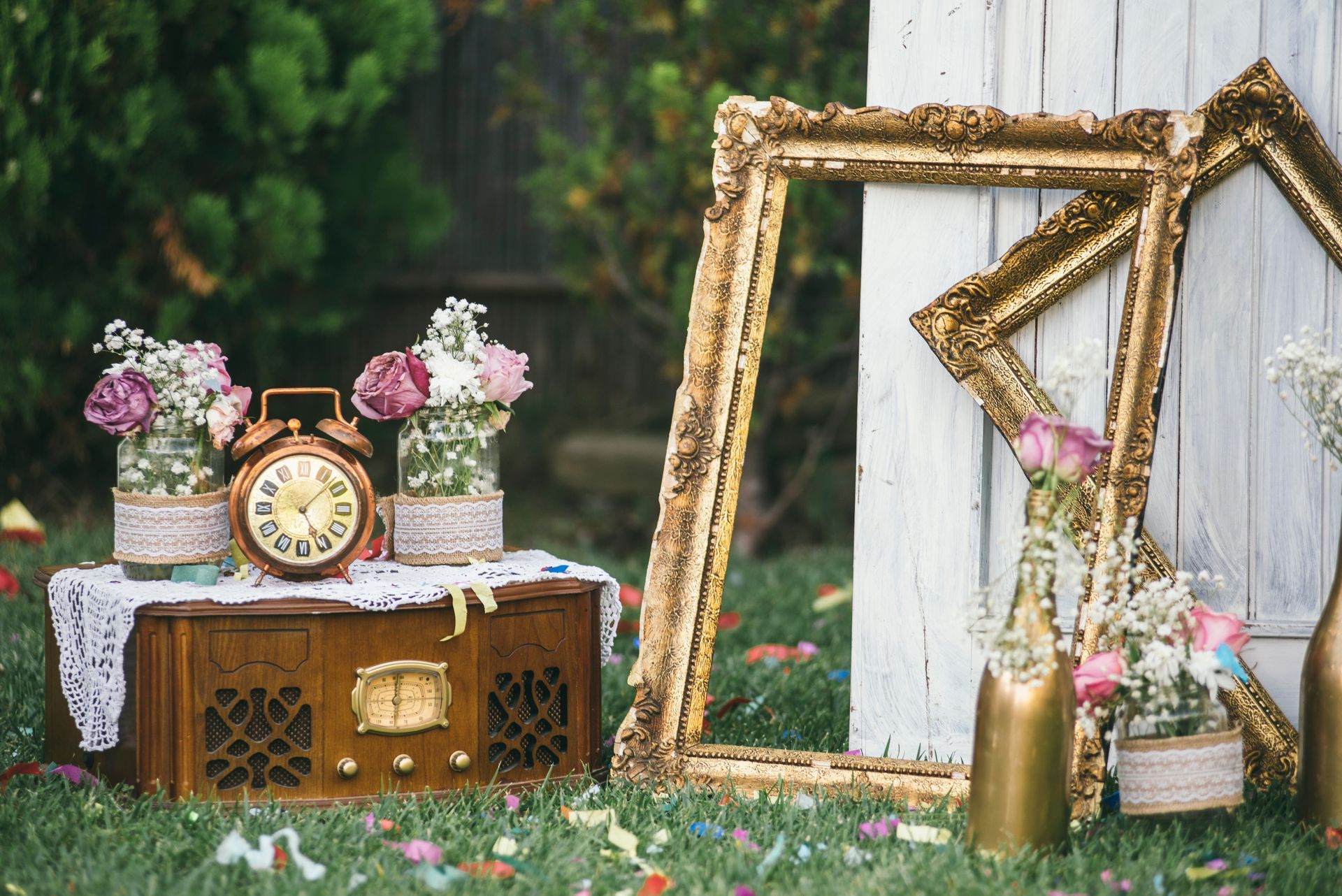 Vintage garden decor with a clock, flowers, and gold-framed mirrors on a rustic table outdoors