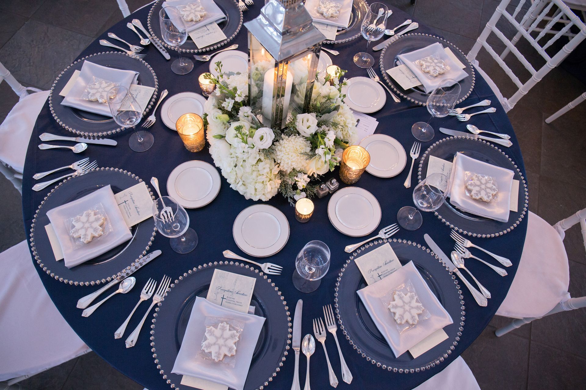 Elegant round banquet table set with navy linens, white floral centerpiece, candles, and neatly arranged place settings