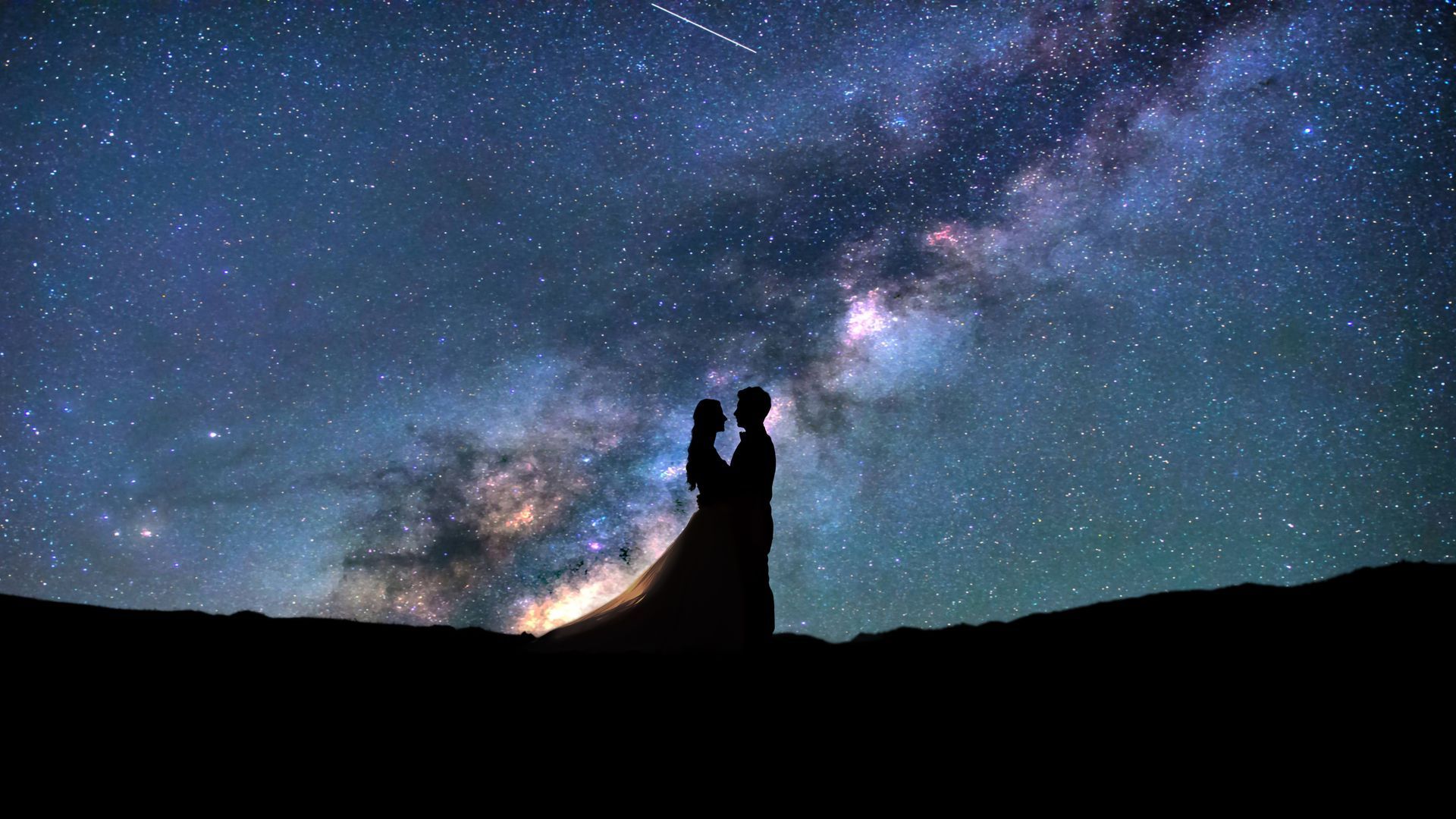Silhouetted couple under a starry Milky Way sky at night