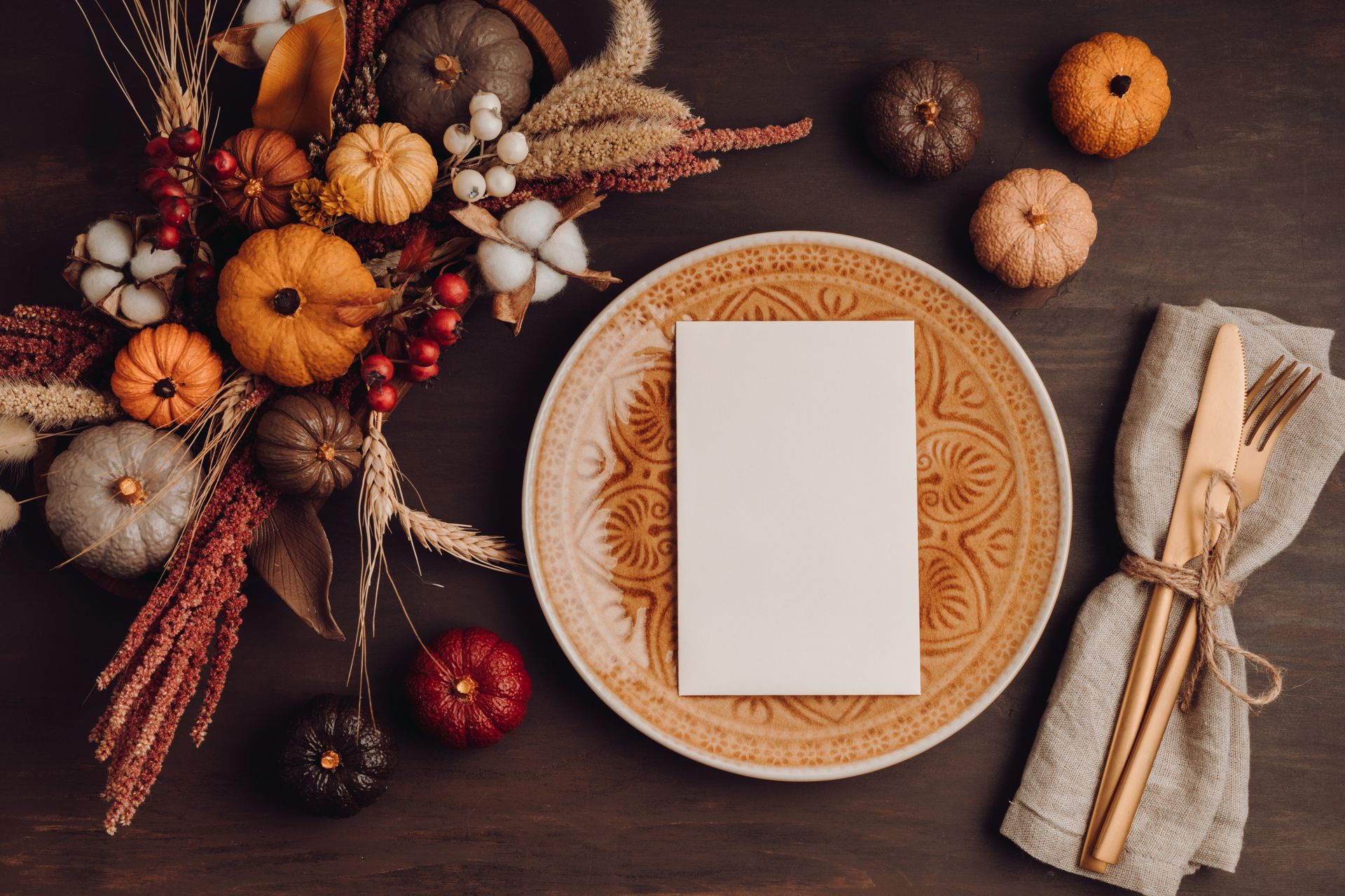Autumn Thanksgiving table setting with pumpkin centerpiece, candles, and a plated napkin in warm light