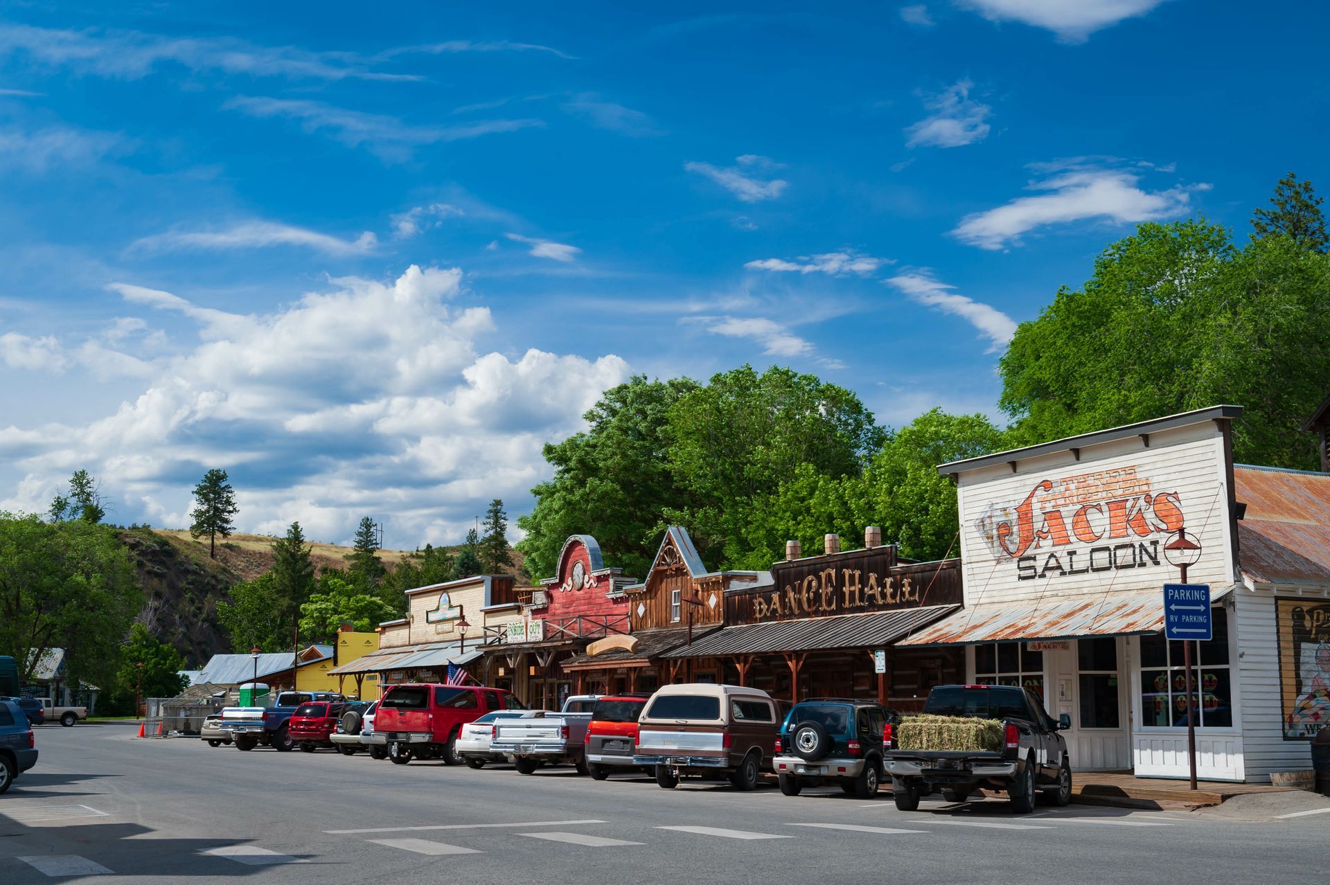 A row of cars are parked on the side of the road in front of a restaurant.