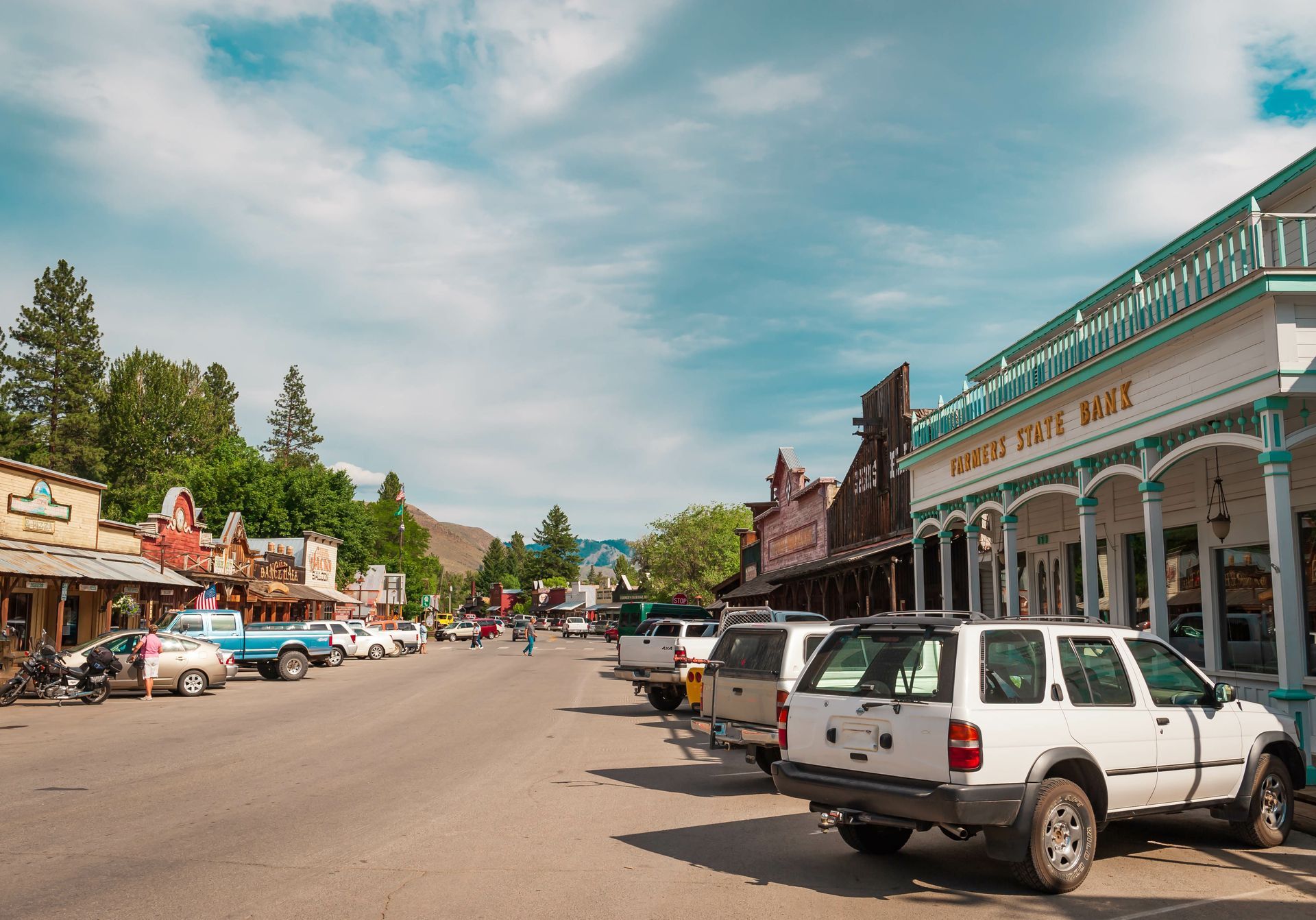 A row of cars are parked on the side of a street in a small town.