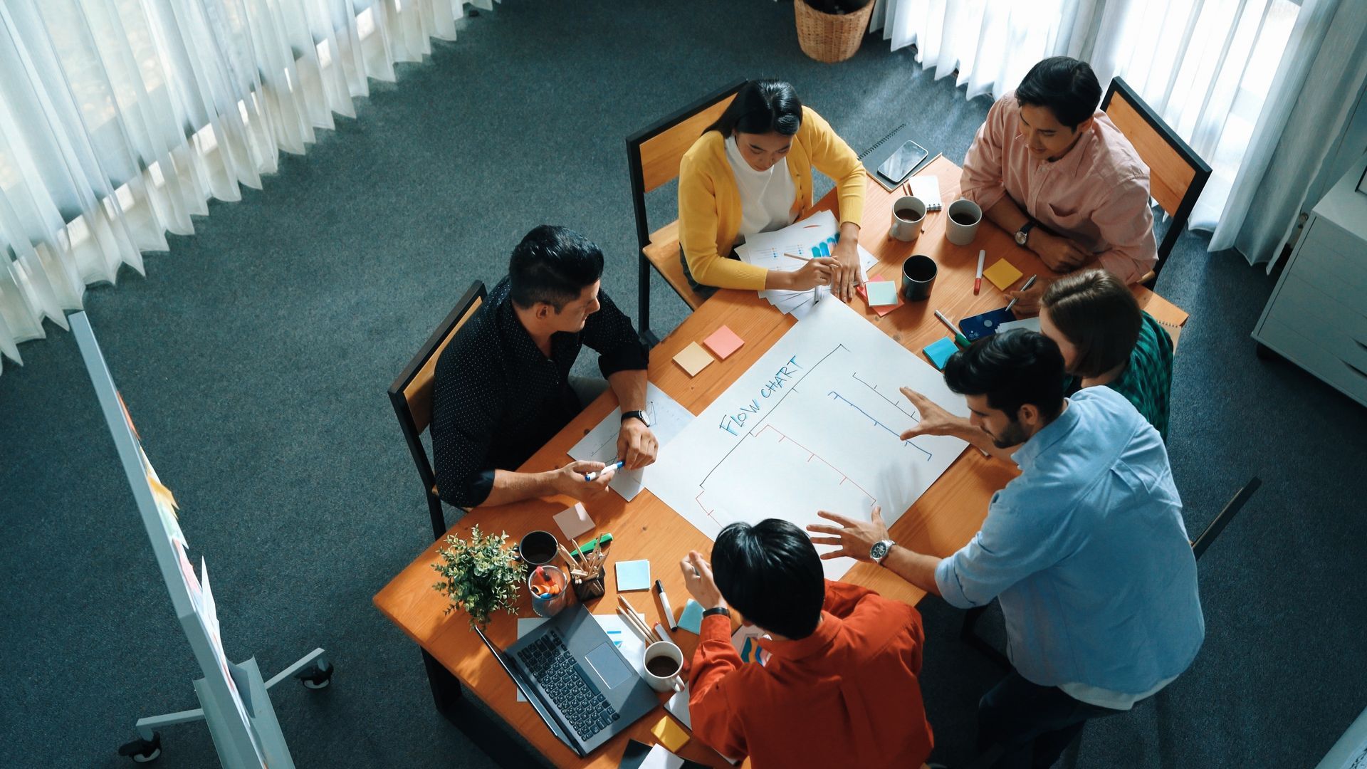 Five people gathered around a table in a bright meeting room, reviewing papers and laptops.
