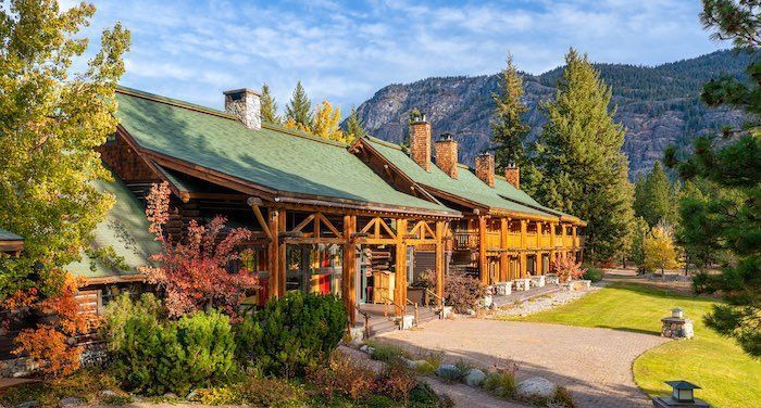 Rustic lodge building with green roof, set against mountain backdrop. Sunny day.