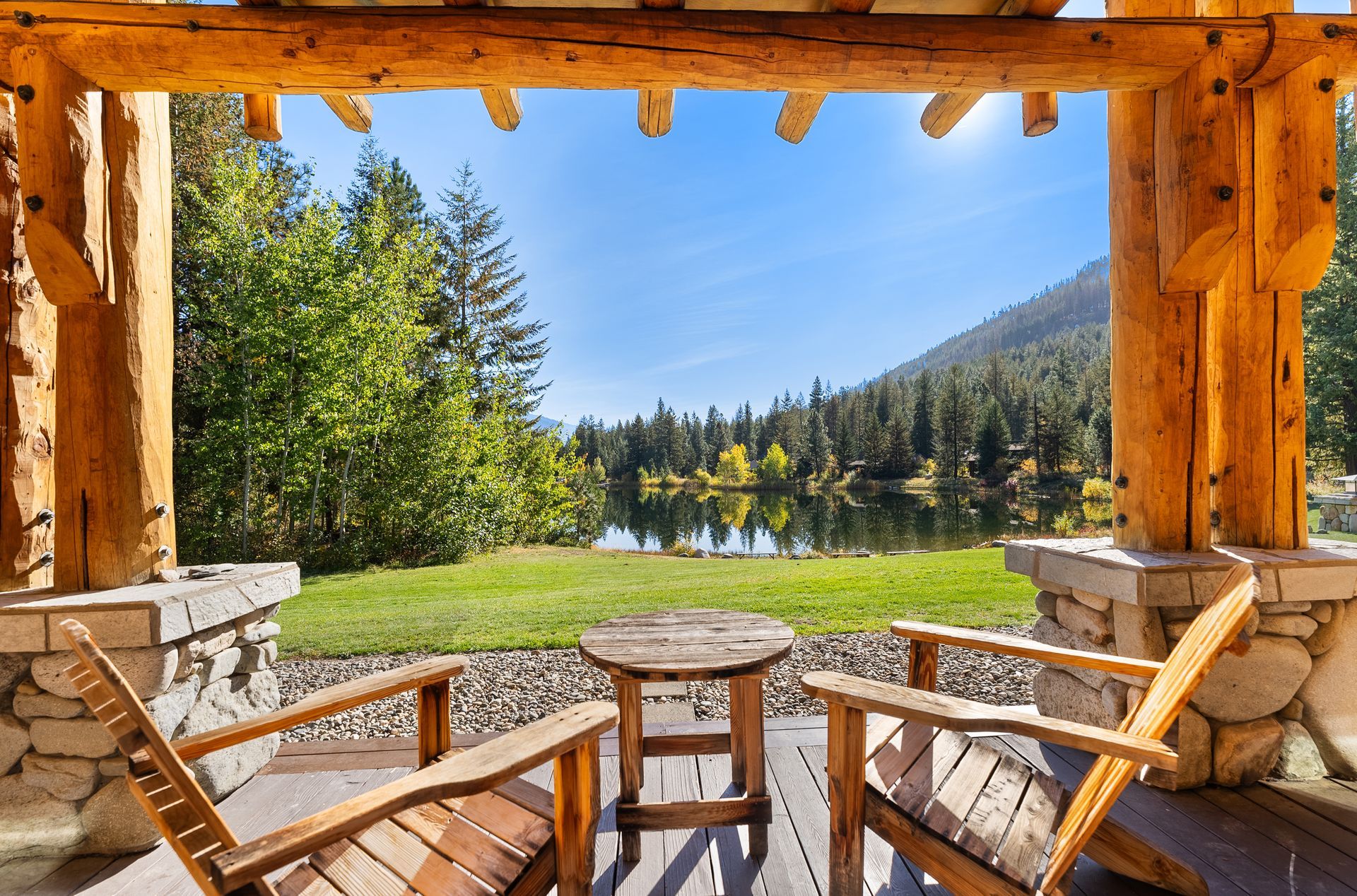 Two wooden chairs are sitting on a porch overlooking a lake.