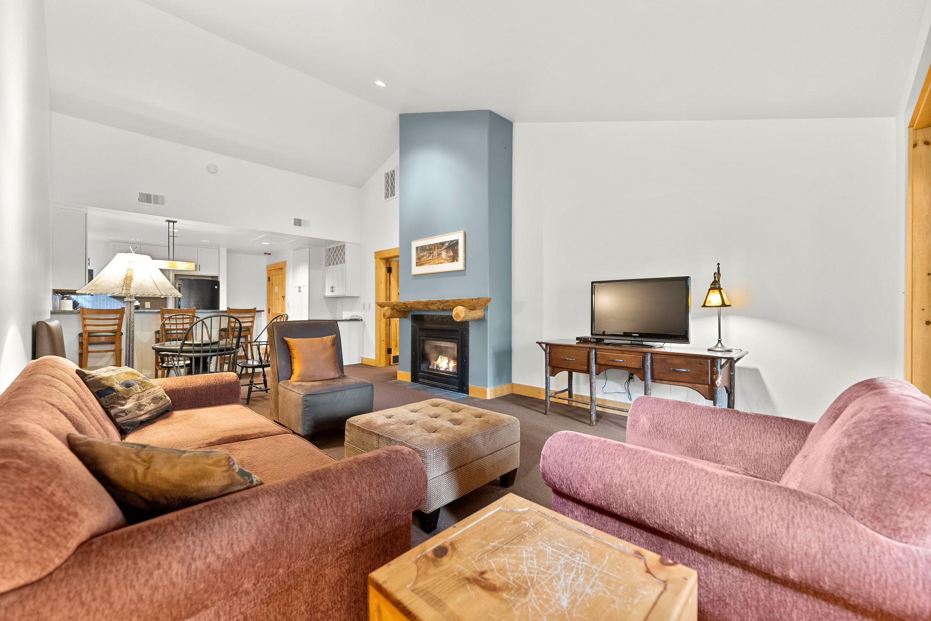 A living room with a couch , chair , ottoman , television and fireplace.