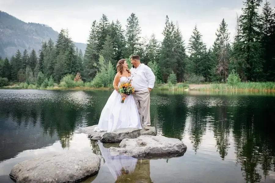 A bride and groom are standing on rocks in the middle of a lake.