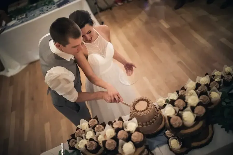 A bride and groom are cutting their wedding cake with cupcakes.