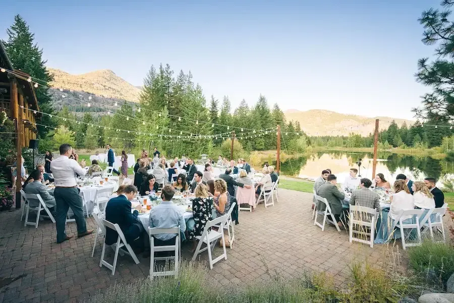 A large group of people are sitting at tables in front of a lake.