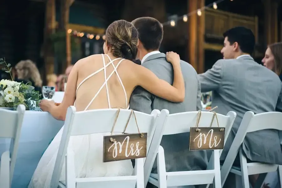 A bride and groom are sitting in chairs at a wedding reception.