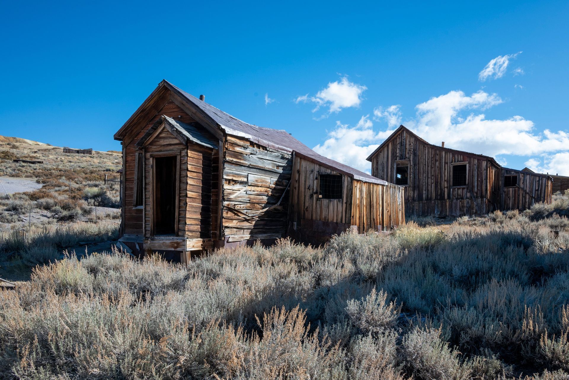 Weathered wooden cabins in a dry, scrubby field under a bright blue sky