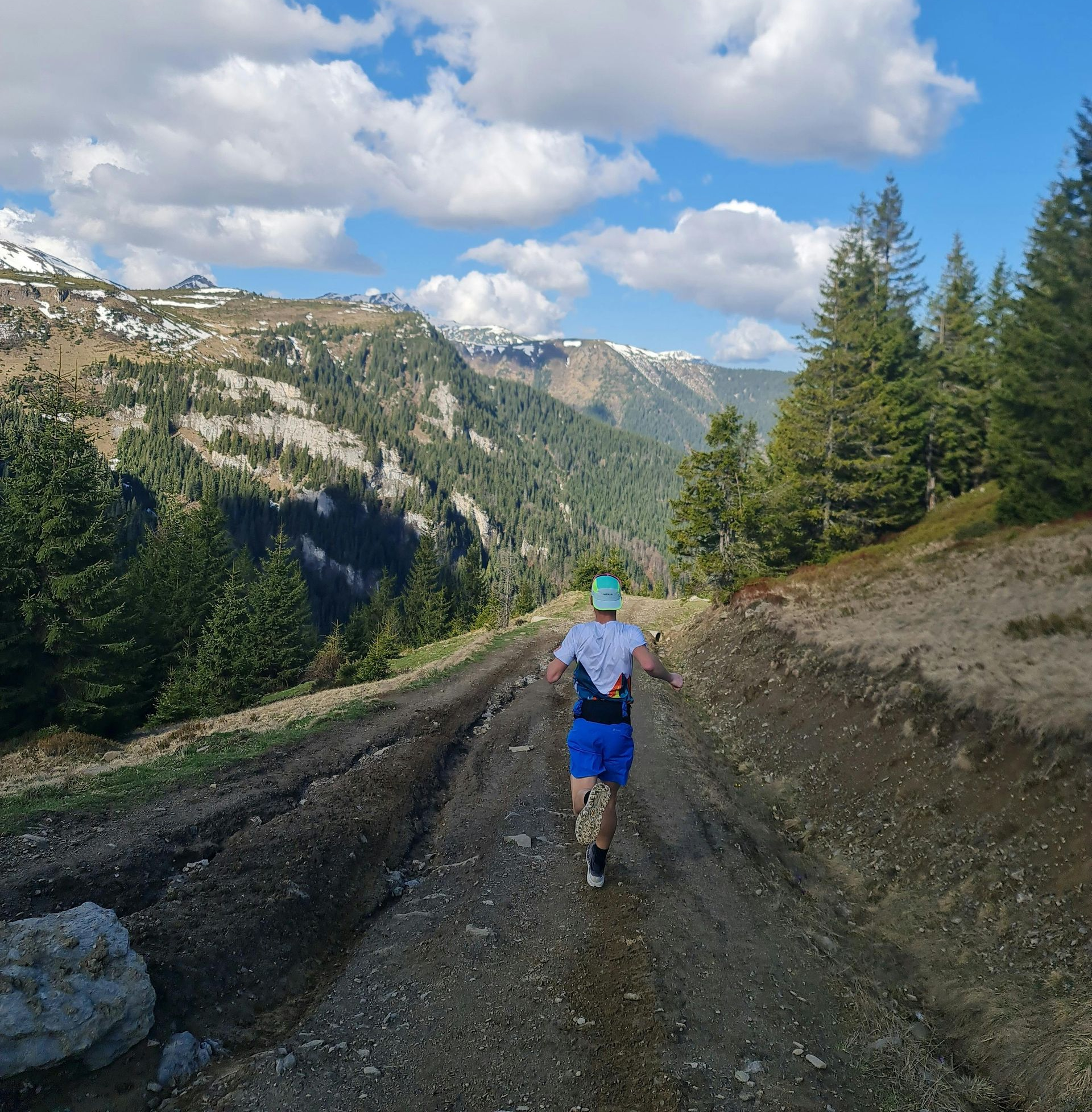 A runner on a dirt trail in a mountain valley under a partly cloudy sky.