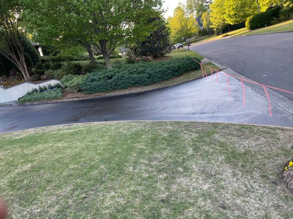 A paved driveway entrance meeting a road with orange survey flags placed along the curb line in a residential yard. A paved driveway entrance meeting a road with orange survey flags placed along the curb line in a residential yard.